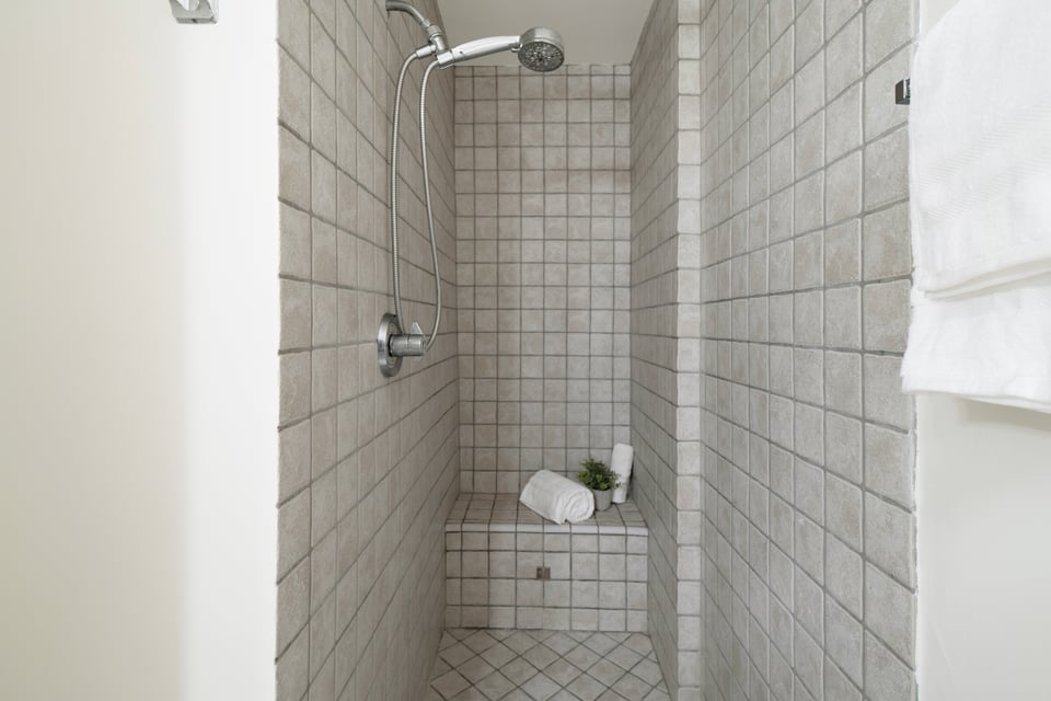 Walk-in shower with gray tile, a built-in bench, handheld showerhead, and folded towels.