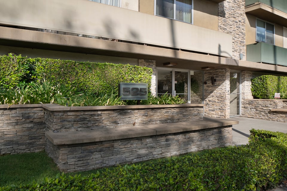 Apartment building entrance with stone facade, landscaped planters, and a sign marked 525.