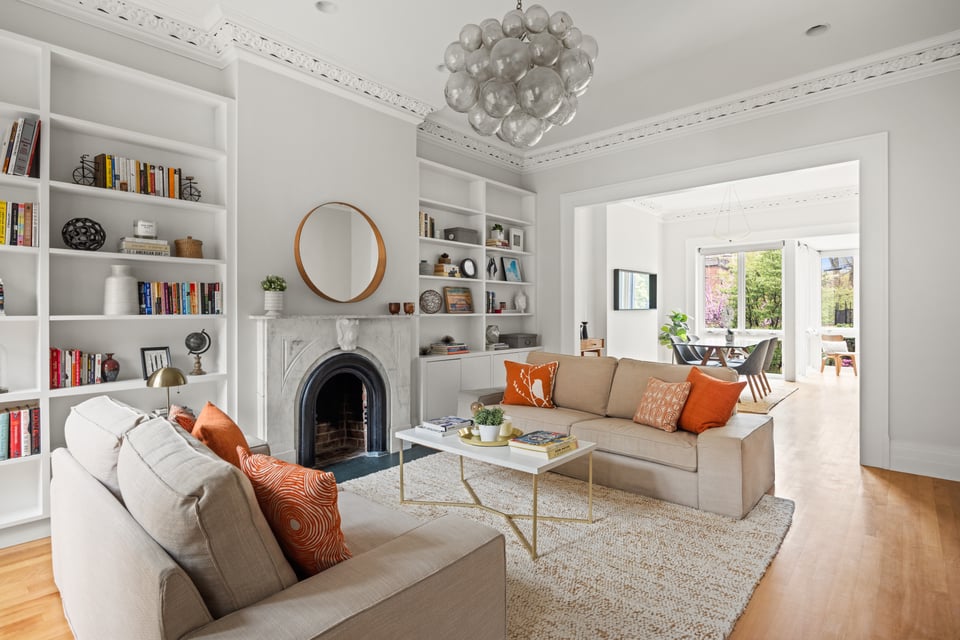 Living room with built-in bookshelves, a marble fireplace, beige sofas, and orange accent pillows.