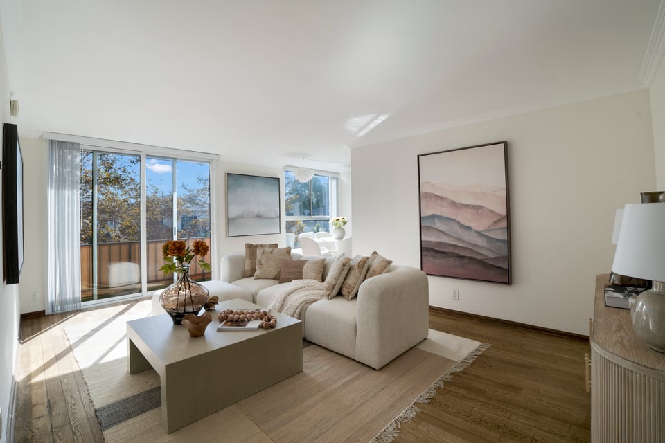 Living room with a cream sectional, neutral artwork, wood floors and sunny sliding glass doors.
