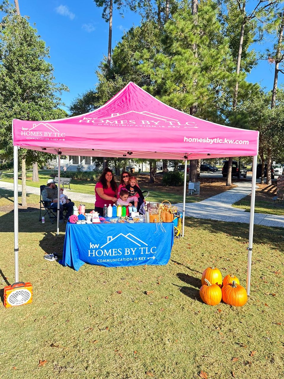 Homes by TLC event booth with a pink canopy, refreshments, and pumpkins in a park.