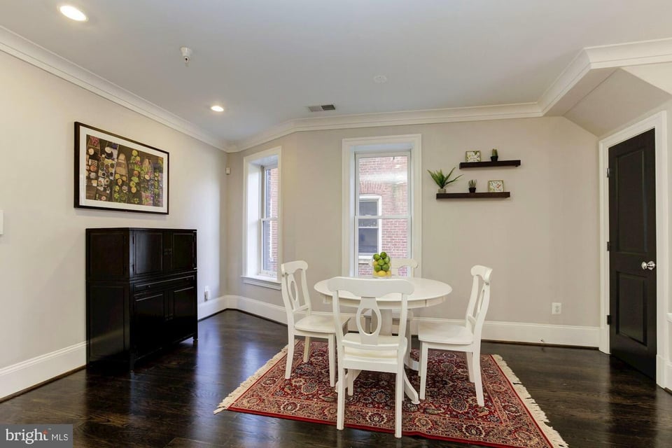 Dining room with a white table and chairs on a patterned rug beside two windows.