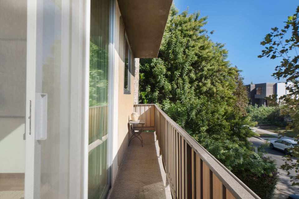 Apartment balcony with a small table and leafy trees beyond the railing.