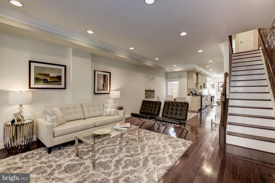 Living room with a white sofa, black leather chairs, hardwood floors, and an open staircase.