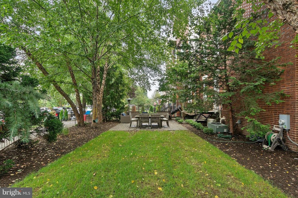 Leafy backyard courtyard with a lawn, mature trees, and a furnished stone patio.