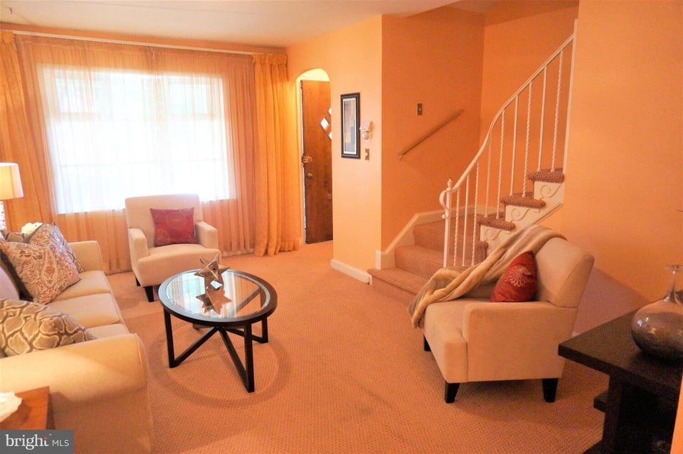 Living room with peach walls, a large curtained window, and a carpeted staircase.