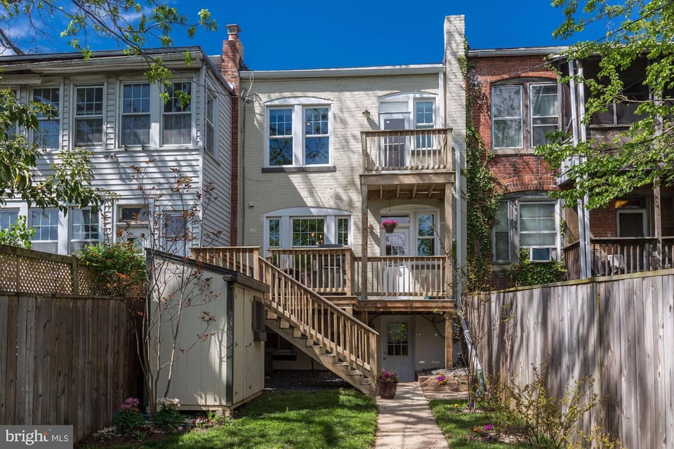 Rear of a light-colored row house with a two-level wooden deck and staircase to the yard.