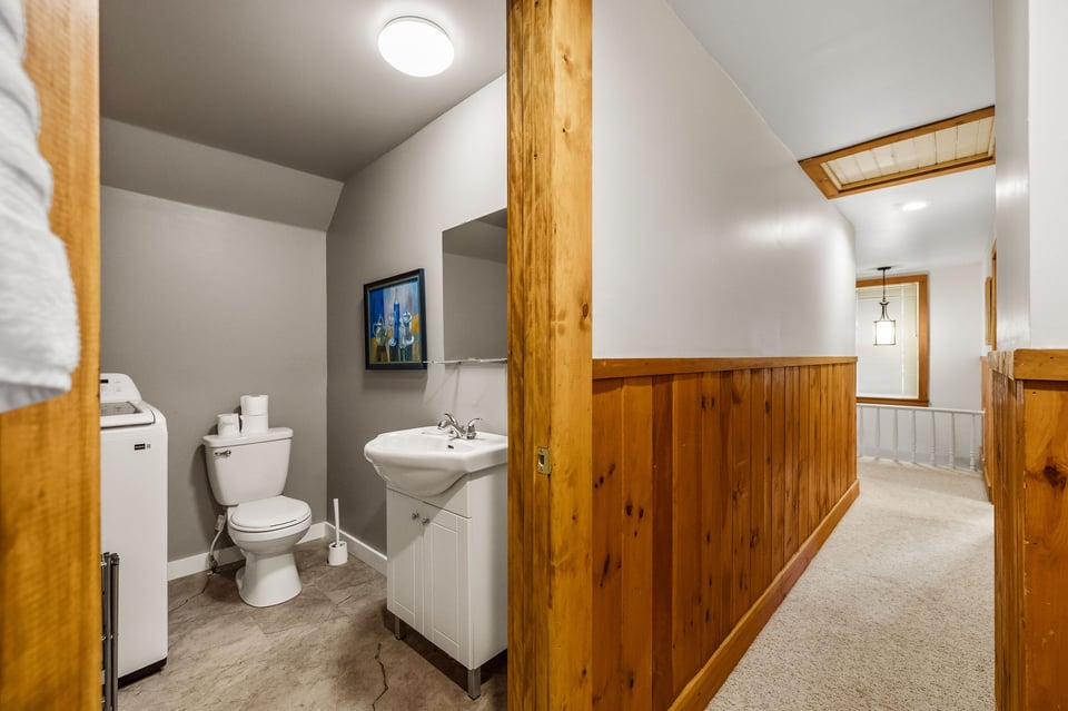 Bathroom and laundry area beside a hallway with warm wood wainscoting.