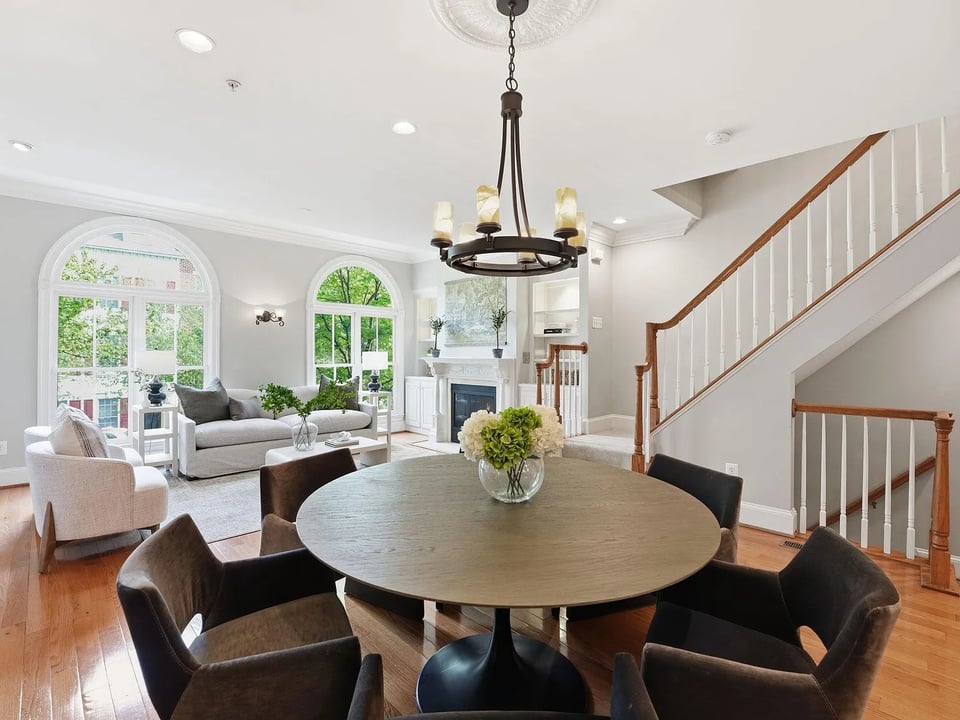 Living and dining room with arched windows, a fireplace, and a sweeping staircase.