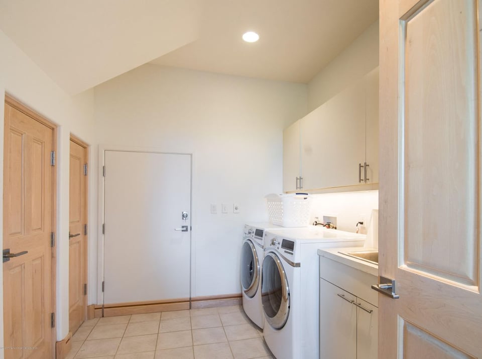 Laundry room with front-loading washer and dryer, white cabinets, and tiled floor.