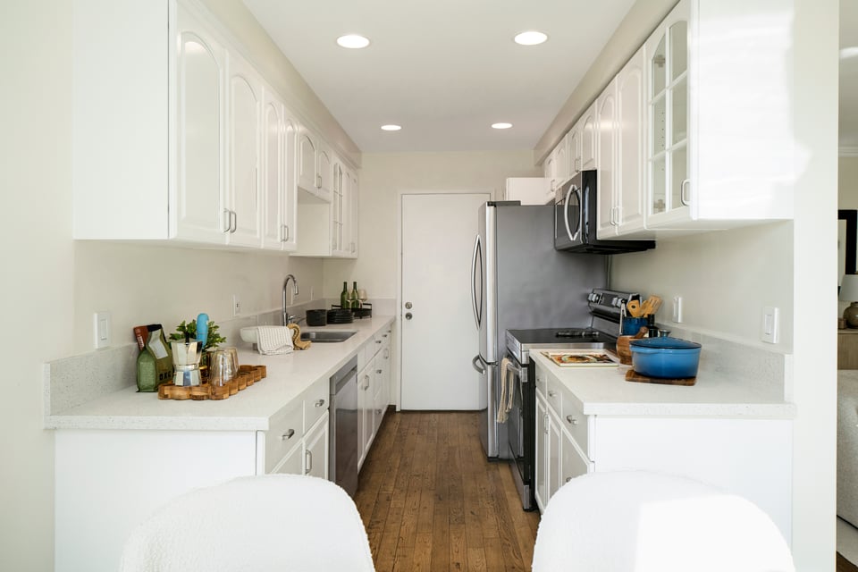 Galley kitchen with white cabinets, stainless steel appliances, pale countertops, and wood flooring.