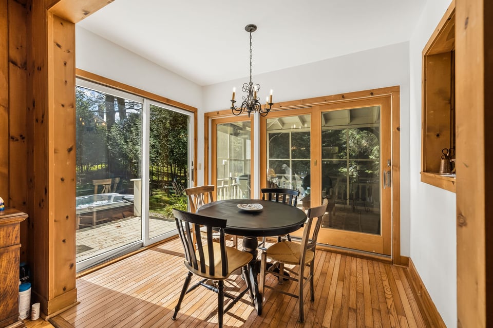 Dining room with a round table, wood floors, and glass doors overlooking a deck and trees.