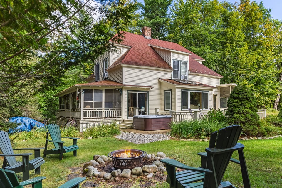 Camp Woodbine’s wooded backyard with a screened porch, hot tub, fire pit, and Adirondack chairs.
