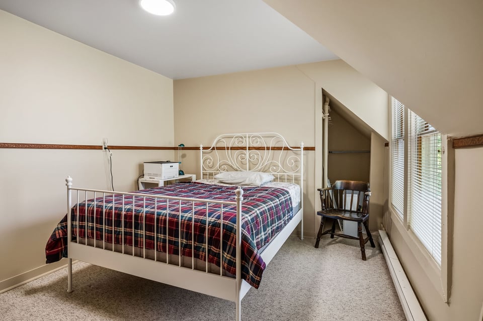 Bedroom with a white metal bed, plaid bedding, and windows beneath a sloped ceiling.