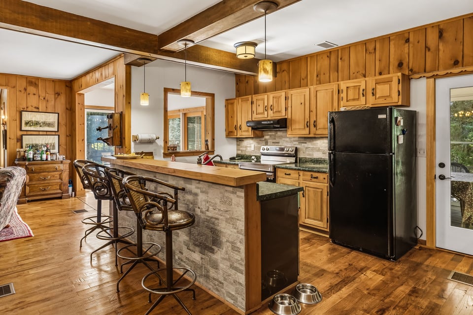 Wood-paneled kitchen with a stone-sided island, bar stools, and black appliances.