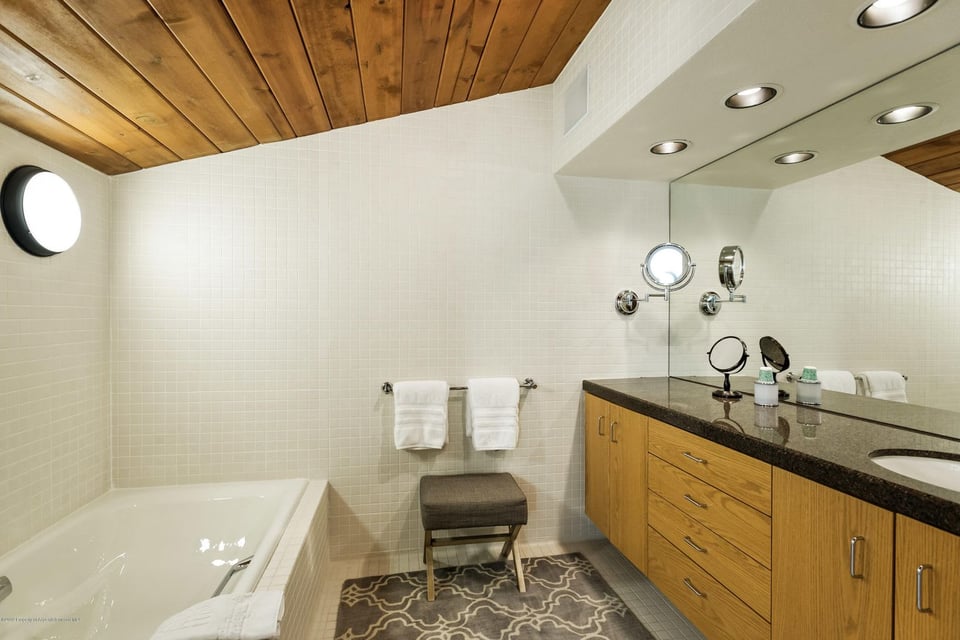 Bathroom with a built-in tub, wood ceiling, and long wood vanity with a dark countertop.