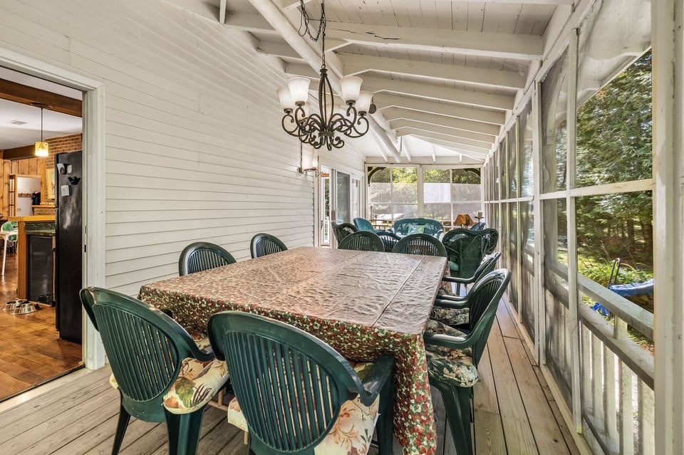 Screened porch dining area with a long table, green chairs, and leafy views.