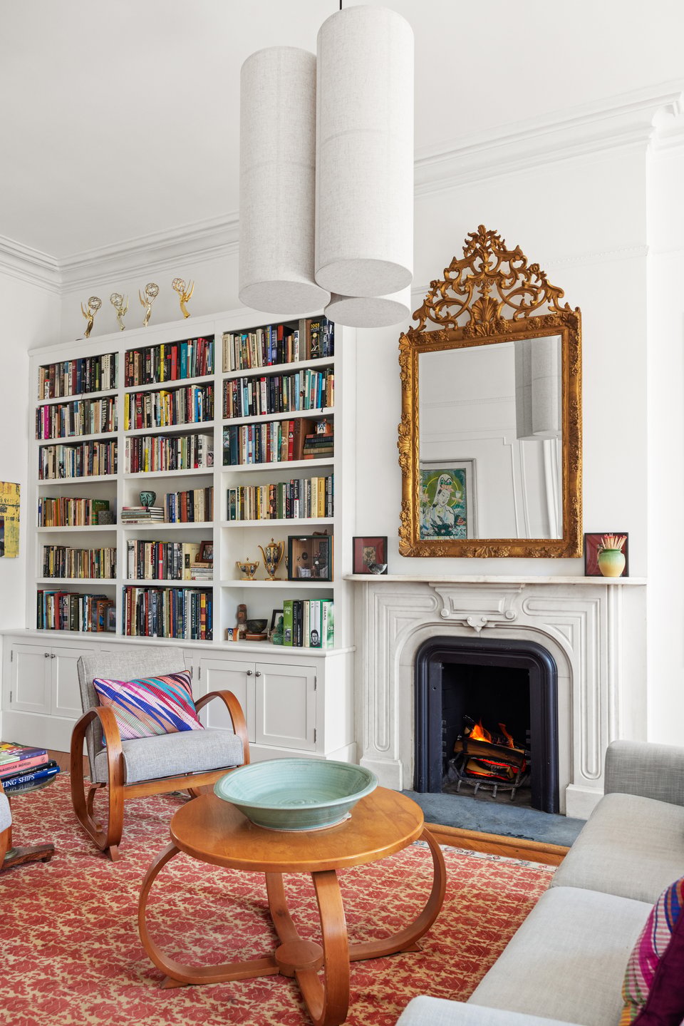Living room with book-filled built-ins, a lit fireplace, and an ornate gold mirror.