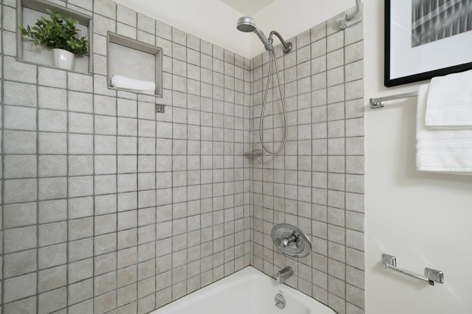 Tiled bathtub shower with a handheld showerhead and recessed shelves.