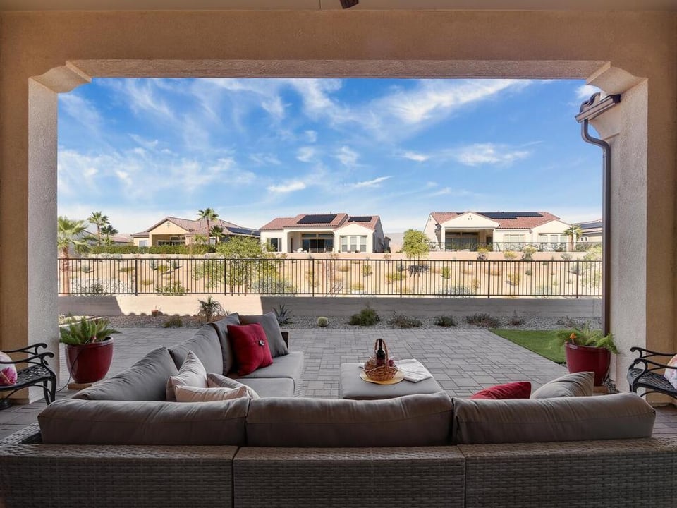 Covered patio with sectional seating and paver flooring, overlooking desert landscaping and neighboring homes.