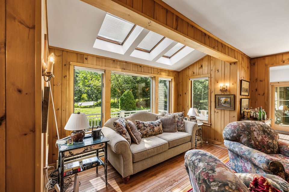 Living room with pine walls, three skylights, broad windows, hardwood floors, and floral armchairs.