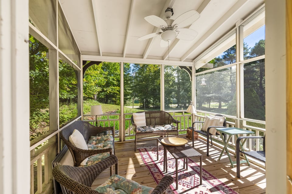 Screened porch with wicker seating, a ceiling fan, and views of leafy trees.