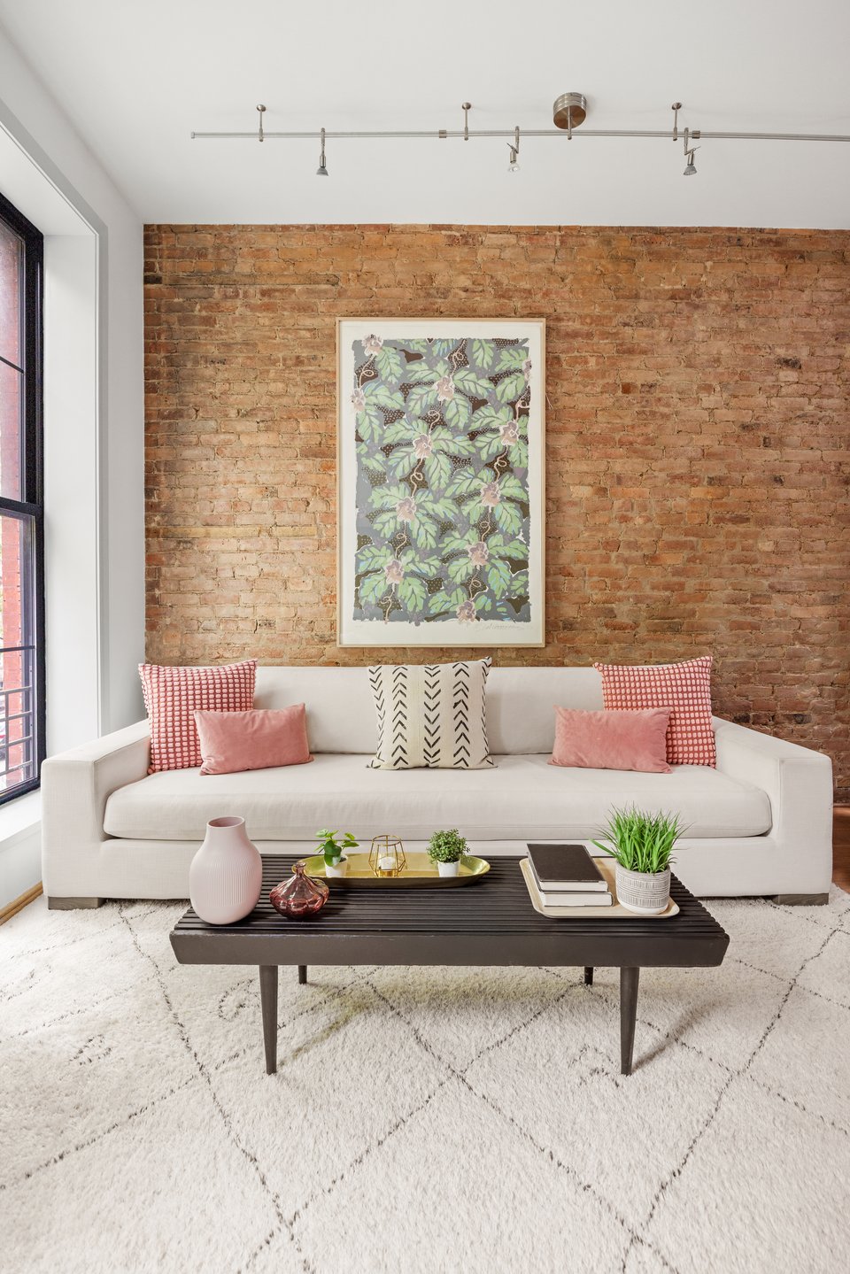 Living room with a white sofa against an exposed brick wall and framed botanical artwork.