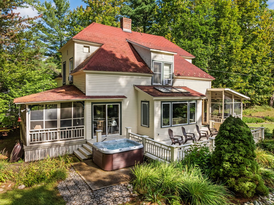 Wooded home with red roof, screened porch, deck seating, and a hot tub.