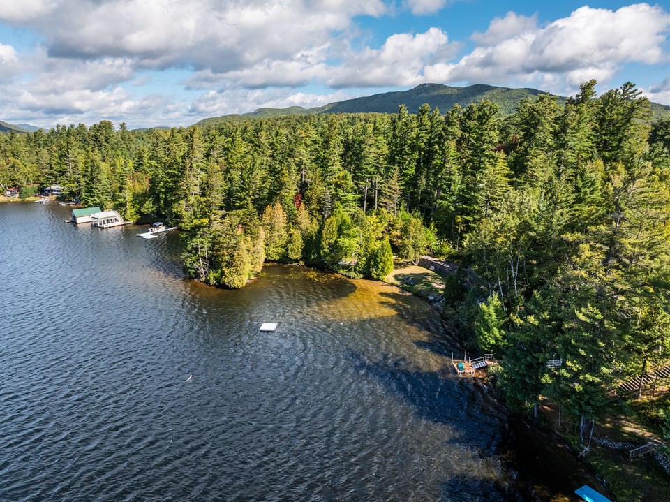 Aerial lakefront view with docks, wooded shoreline, and forested mountains.