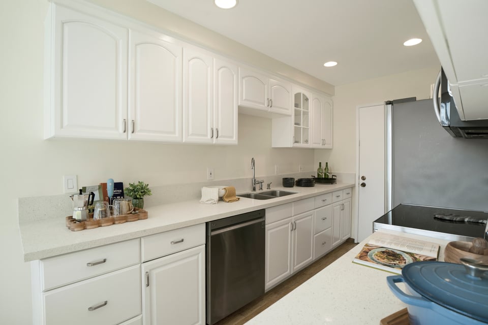 Kitchen with white paneled cabinets, light counters, stainless-steel dishwasher, and blue Dutch oven.