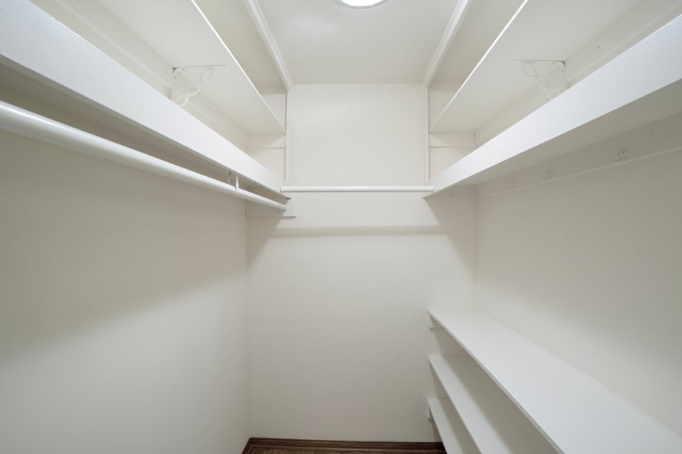 Empty walk-in closet with white built-in shelving on three sides.