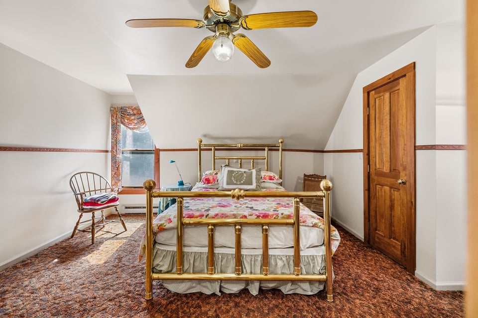 Bedroom with a brass bed, floral bedding, patterned carpet, and wooden door.