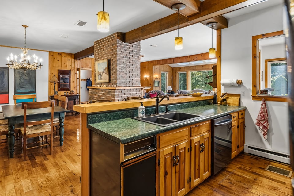 Rustic kitchen with green countertops, a wood island, exposed beams, and a brick chimney.