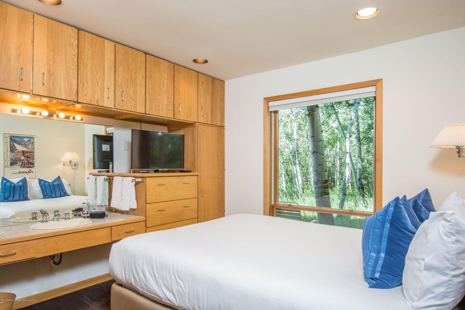 Bedroom with built-in wood cabinets, a vanity sink, and a large window overlooking trees.