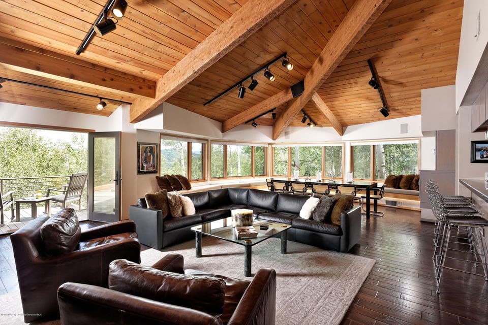 Living room with exposed wood beams, expansive windows, and black leather seating.