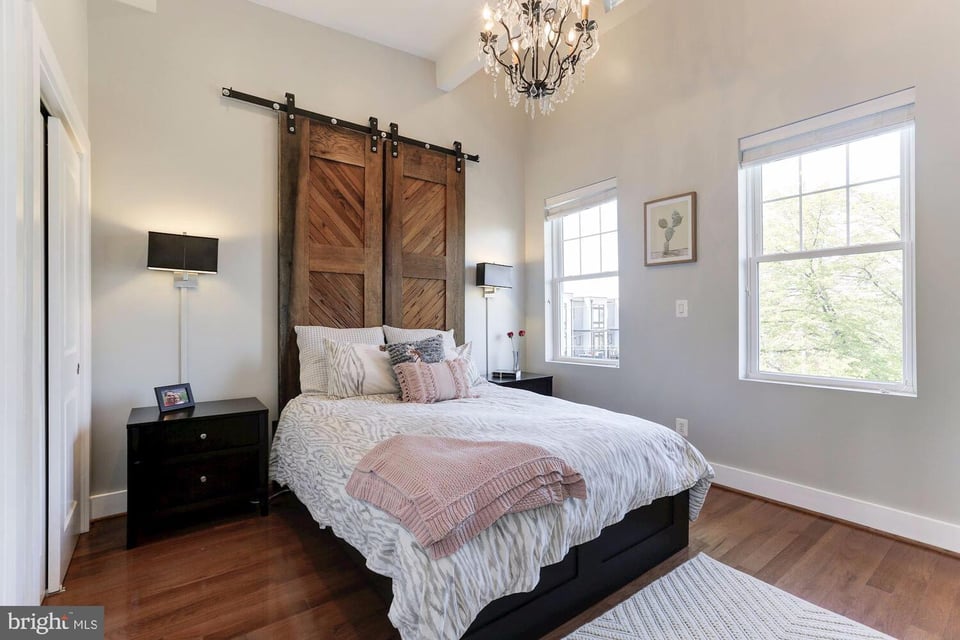 Bedroom with rustic sliding barn doors behind the bed and tall windows.