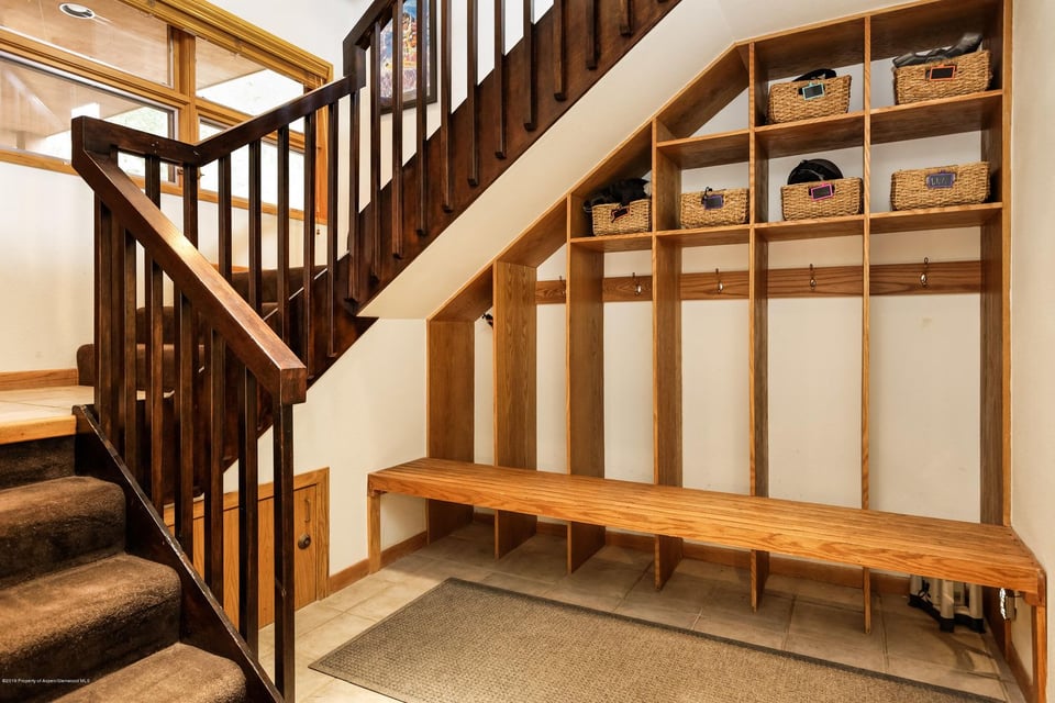 Mudroom with a dark wood staircase, built-in cubbies, wicker baskets, hooks, and a long wooden bench.