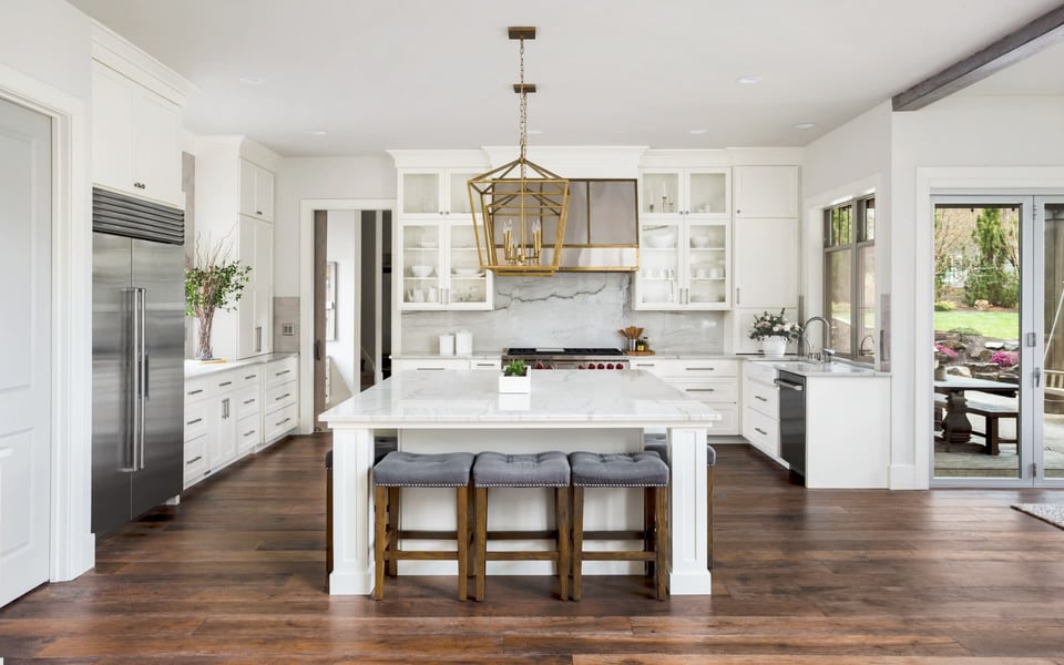 A well-lit kitchen with a large center island, stainless steel appliances, wood cabinets, a dining table, and chairs in Bergen County