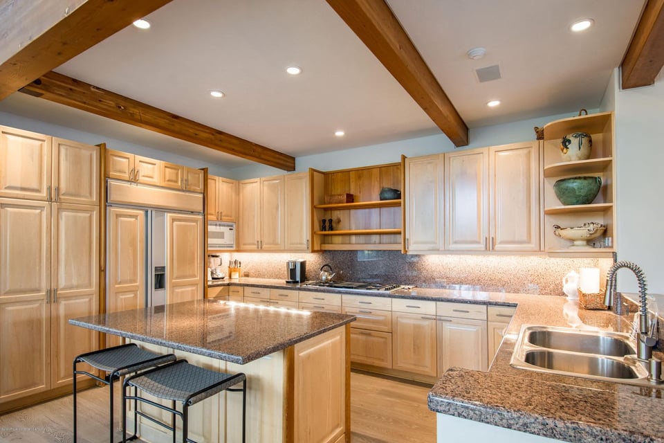 Kitchen with a granite island, light wood cabinets, and exposed ceiling beams.
