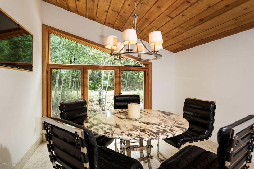 Dining room with a round marble table, black leather chairs, and a vaulted wood ceiling.