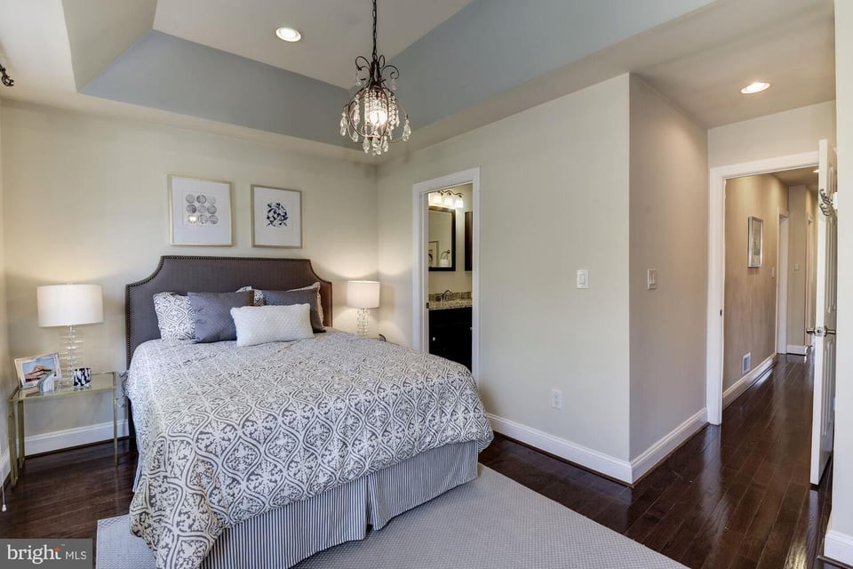 Bedroom with a patterned bed, chandelier, tray ceiling, and dark hardwood floors.