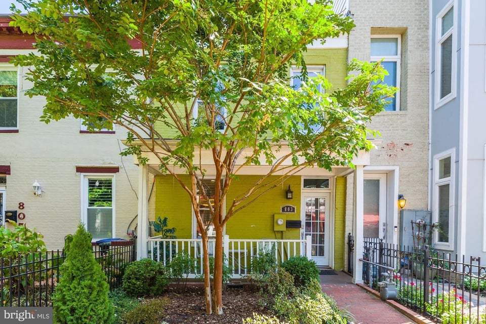 Townhouse with a lime-green facade, covered porch, and leafy tree in front.