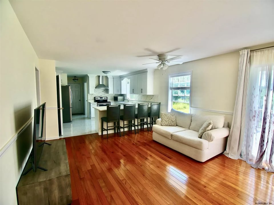 Open-plan living room and kitchen with hardwood floors, a cream sofa, and a breakfast bar.