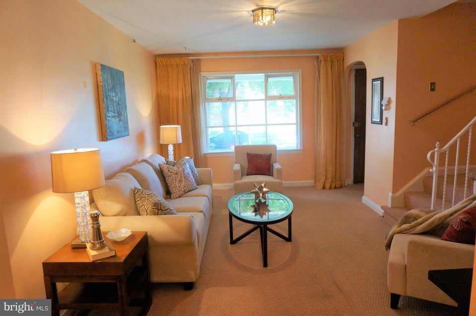 Living room with beige sofas, a glass coffee table, and a large curtained window.