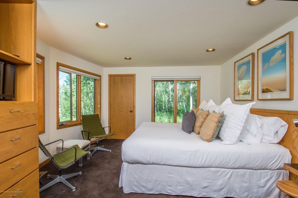 Bedroom with a white bed, wood cabinetry, and windows overlooking trees.