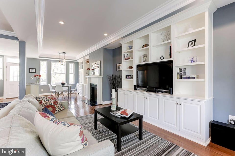 Living room with built-in white TV cabinetry, fireplace, and dining area by the windows.