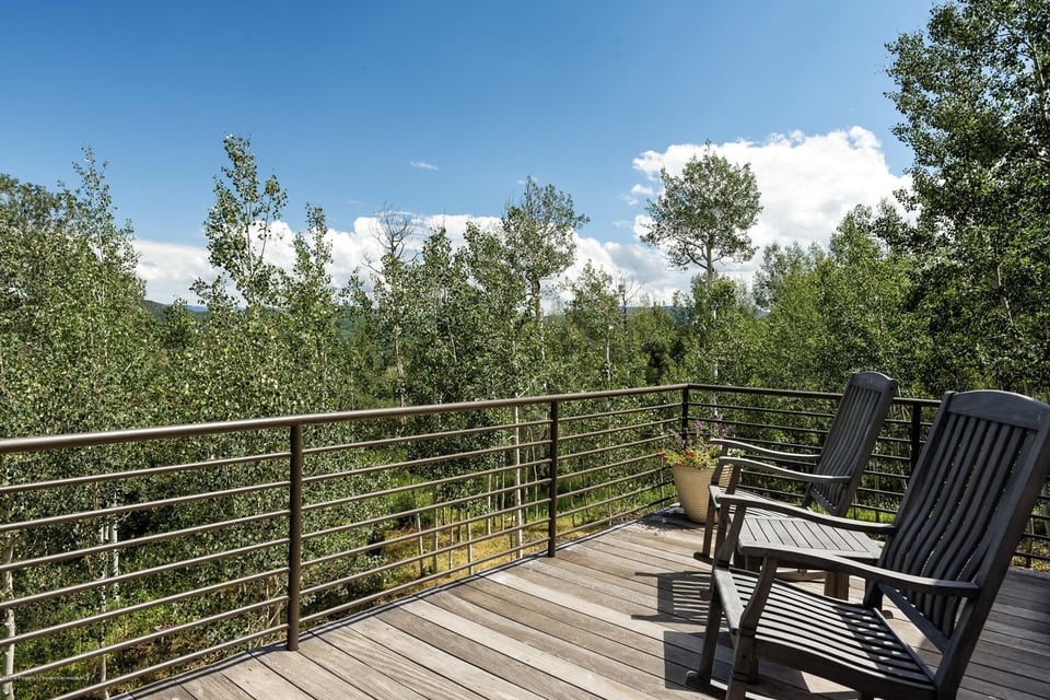 Wooden deck with two Adirondack chairs overlooking leafy trees.