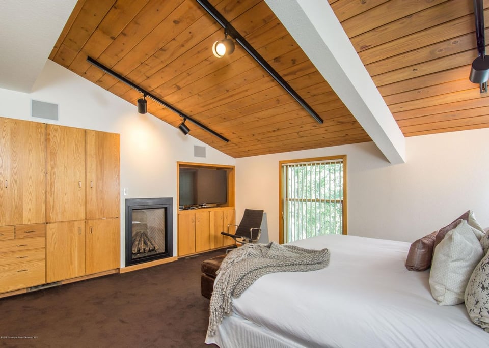 Bedroom with a vaulted wood ceiling, built-in cabinetry, and a fireplace beside the bed.