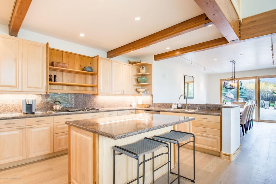 Kitchen with a granite island, light wood cabinets, exposed beams, and glass doors to a patio.