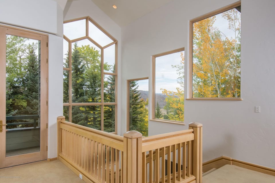 Upstairs landing with a light wood railing and tall windows overlooking autumn trees and mountains.